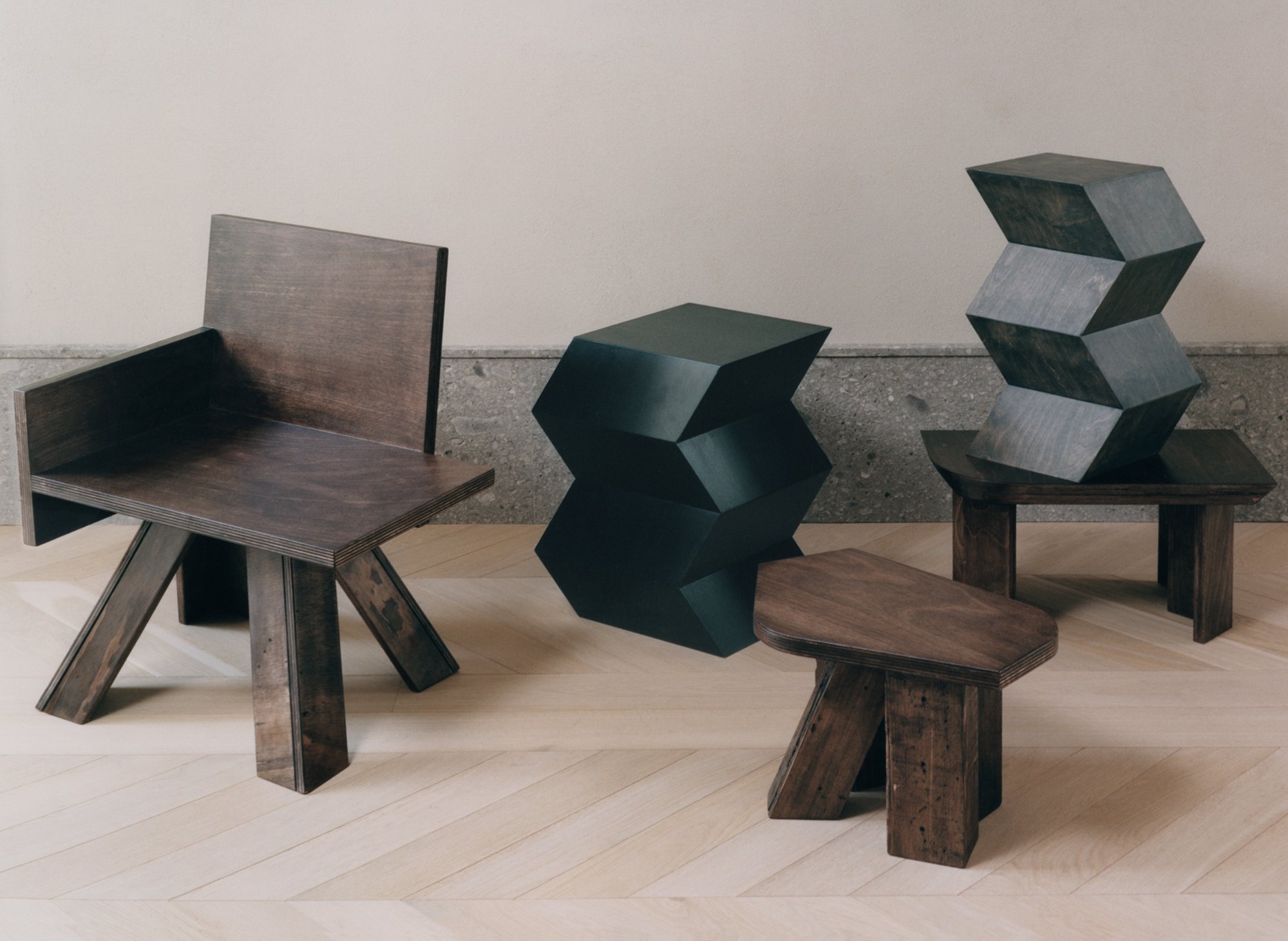 End Table Chair, two Totems, Original Stool and Corner Table by Studio Goons in dark-stained wood on a herringbone floor.