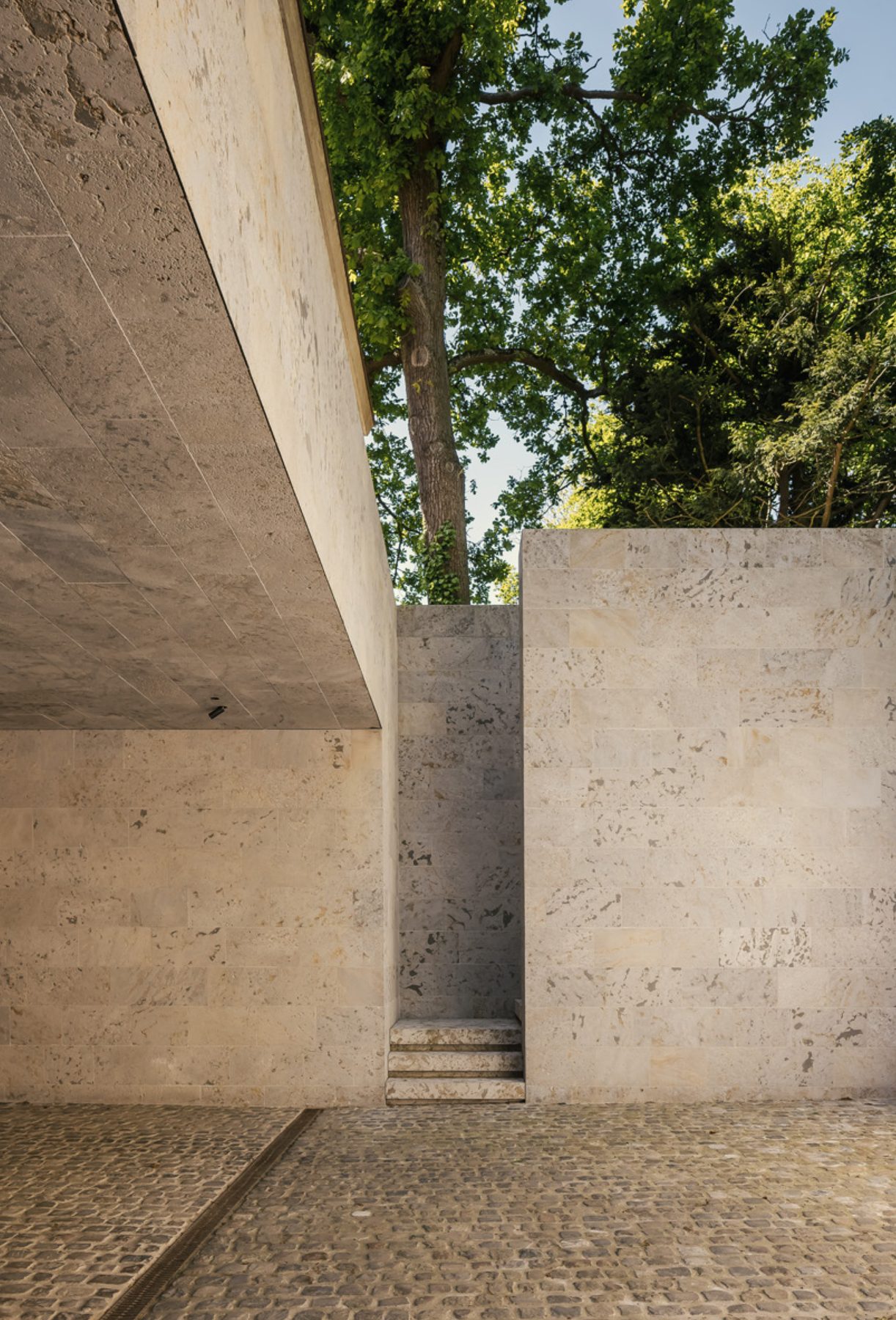 Courtyard of the VC House by Simon de Burbure in Knokke, stone walls and a deep overhang with oak trees beyond, photograph by Cafeine.