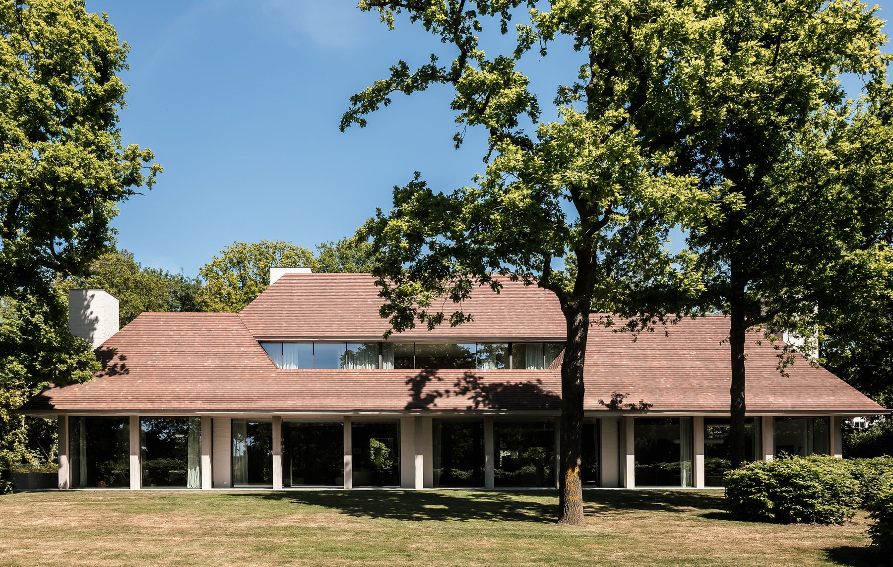 The VC House by Simon de Burbure in Knokke seen from the garden, a long tiled roof over a row of pale columns, photograph by Cafeine.